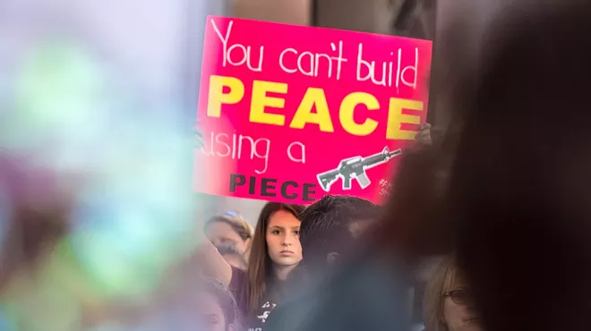 A girl holds a poster that reads "You can't build peace using a piece" with a photo of a gun.