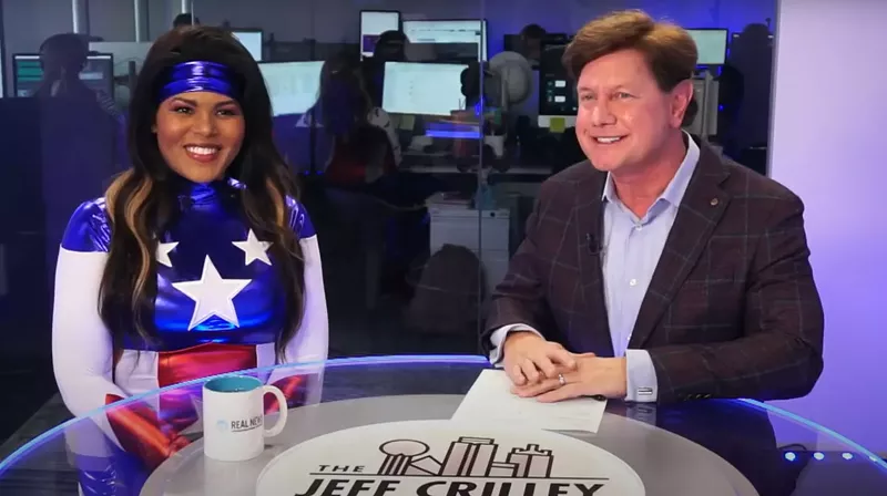 Image: Raven Harrison is wearing a Wonder Woman suit, looking at the camera. She sitting on the left of Jeff Crilley.