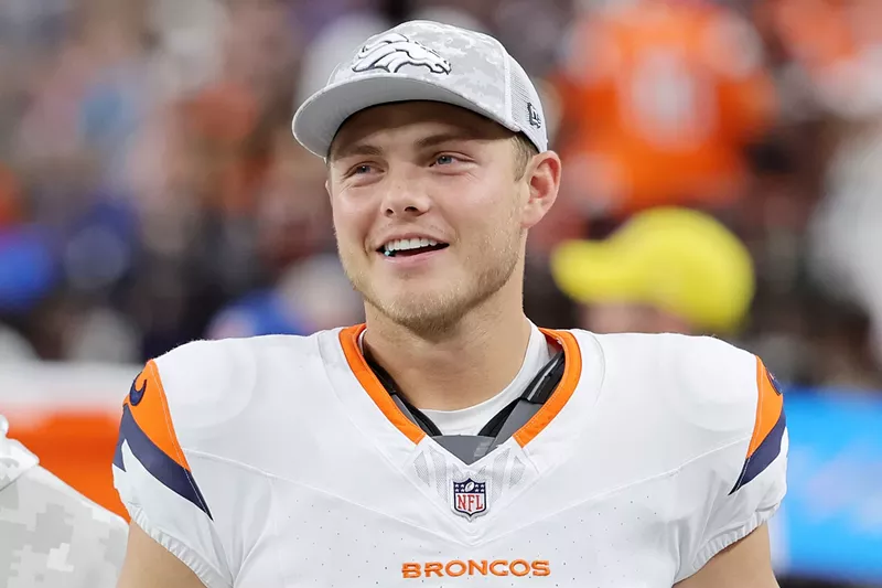 Image: Candid photo of a smiling Zach Wilson #4 of the Denver Broncos in uniform but wearing a team ballcap and looking on during the third quarter of a game against the Las Vegas Raiders at Allegiant Stadium in Las Vegas, Nevada, on November 24, 2024.