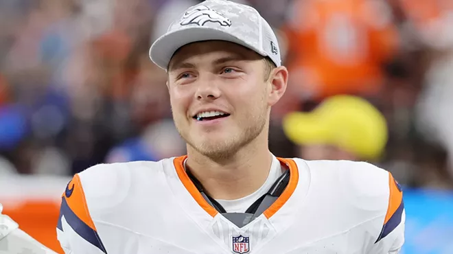 Candid photo of a smiling Zach Wilson #4 of the Denver Broncos in uniform but wearing a team ballcap and looking on during the third quarter of a game against the Las Vegas Raiders at Allegiant Stadium in Las Vegas, Nevada, on November 24, 2024.