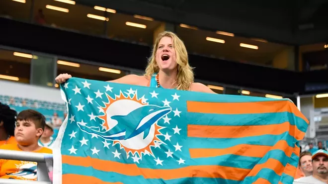 A blonde woman holds a Miami Dolphins flag with teal and orange stripes on it